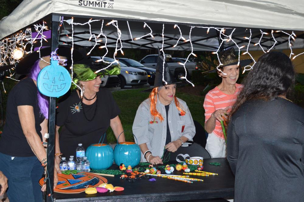 Women wearing witch hats stand behind table with Halloween-themed toys and items